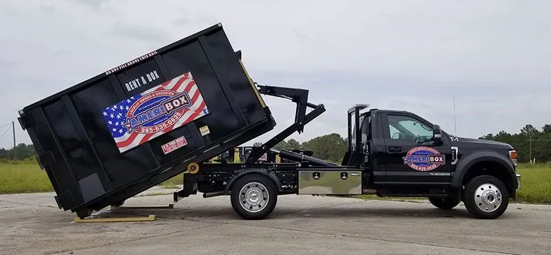 A picture of an Ameribox truck unloading a black Ameribox dumpster in a parking lot.